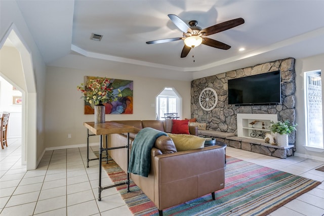 tiled living room featuring ceiling fan, a tray ceiling, and a stone fireplace