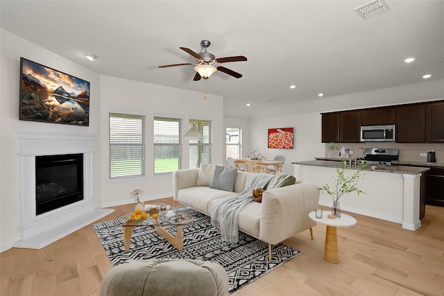 living room with ceiling fan, sink, and light wood-type flooring