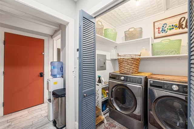 clothes washing area featuring washing machine and dryer, light hardwood / wood-style floors, and electric panel