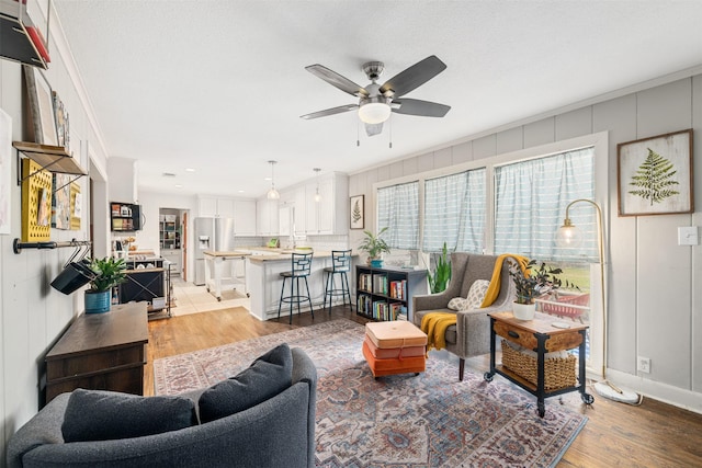 living room featuring crown molding, ceiling fan, and light hardwood / wood-style flooring