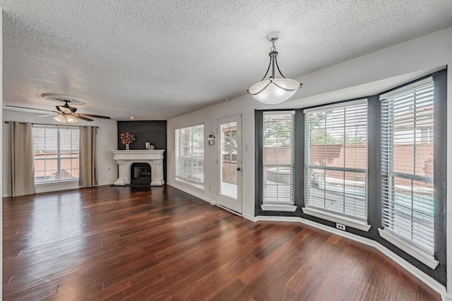 unfurnished living room with a fireplace, dark wood-style flooring, a textured ceiling, and a ceiling fan