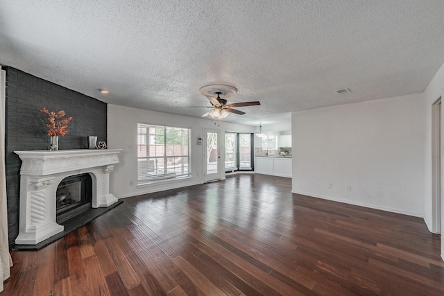 unfurnished living room featuring visible vents, ceiling fan, a fireplace with raised hearth, and a textured ceiling