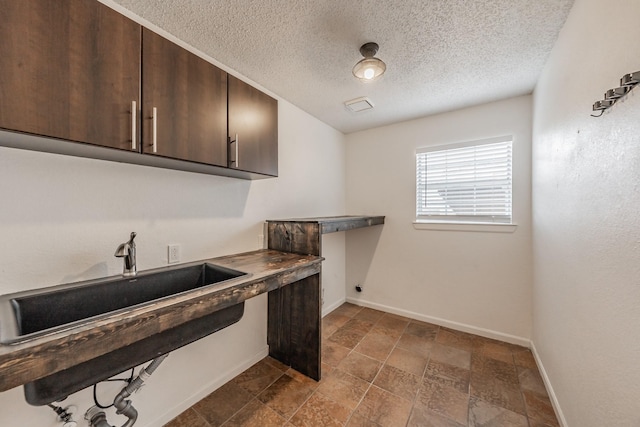 clothes washing area featuring electric dryer hookup, baseboards, a textured ceiling, cabinet space, and a sink
