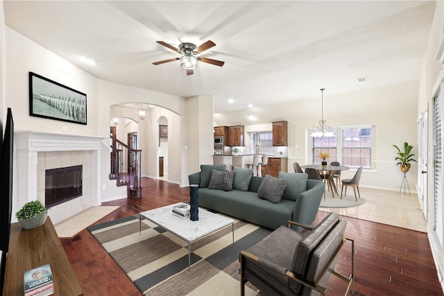 living room featuring a tiled fireplace, ceiling fan with notable chandelier, and light wood-type flooring