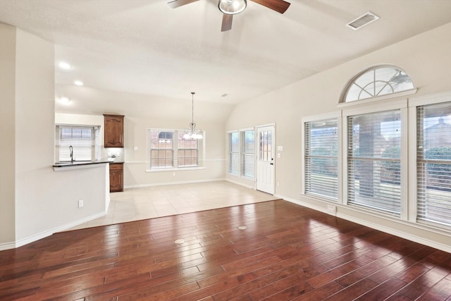 unfurnished living room featuring ceiling fan with notable chandelier, light hardwood / wood-style flooring, and vaulted ceiling