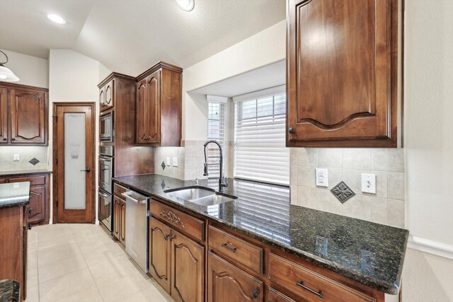 kitchen with sink, vaulted ceiling, light tile patterned floors, dark stone countertops, and appliances with stainless steel finishes