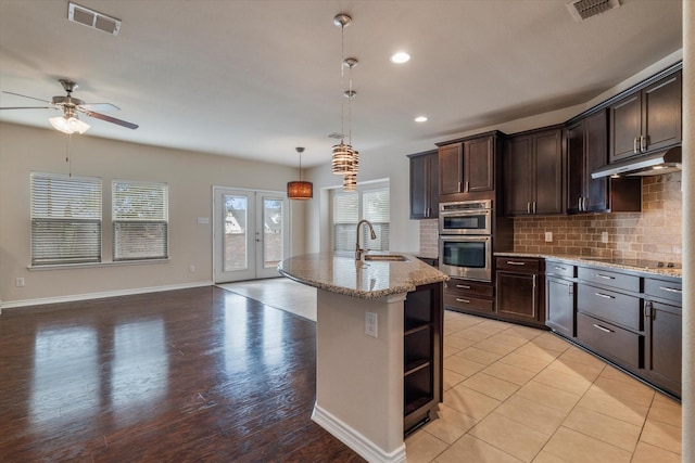 kitchen with pendant lighting, sink, dark brown cabinets, an island with sink, and stainless steel double oven