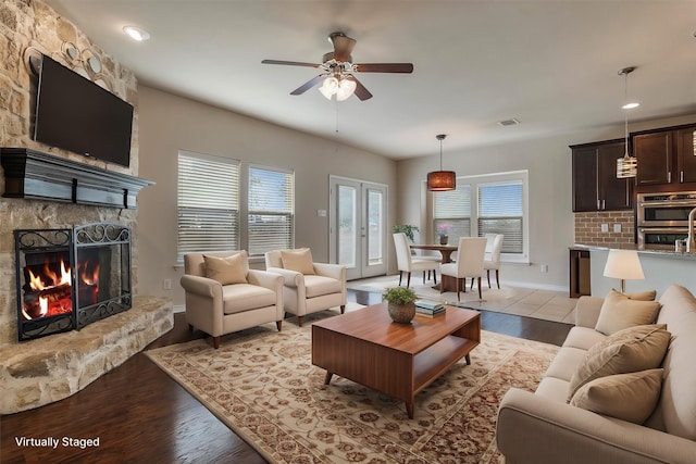 living room featuring ceiling fan, light hardwood / wood-style floors, a fireplace, and french doors