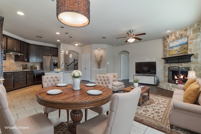 tiled dining room with a stone fireplace and ceiling fan