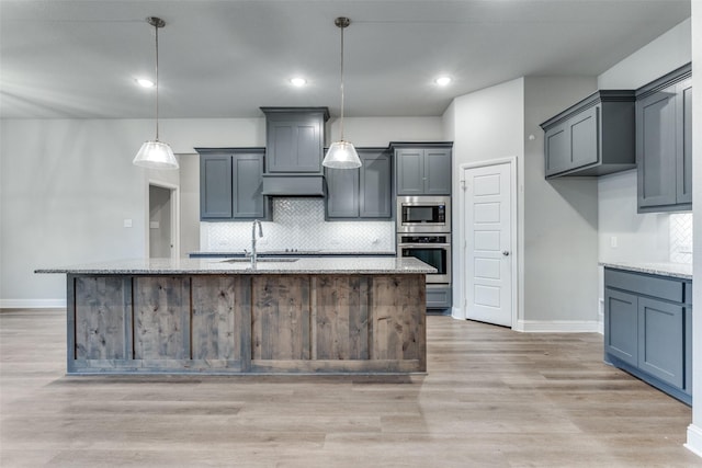 kitchen featuring light stone countertops, a center island with sink, and decorative light fixtures