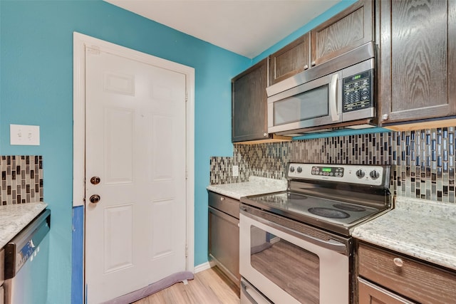 kitchen featuring appliances with stainless steel finishes, backsplash, light stone countertops, dark brown cabinets, and light wood-type flooring