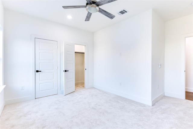 unfurnished bedroom with light carpet, a spacious closet, a closet, and ceiling fan