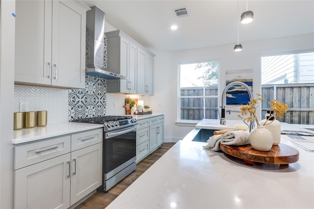 kitchen featuring stainless steel gas stove, decorative backsplash, hanging light fixtures, light stone counters, and wall chimney exhaust hood