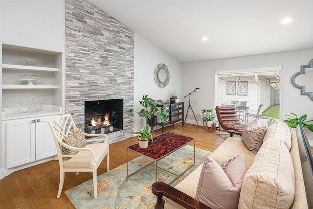 living room with lofted ceiling, built in shelves, a tile fireplace, and light wood-type flooring