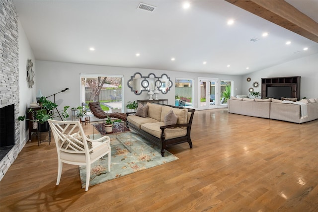 living room with a stone fireplace, lofted ceiling with beams, light hardwood / wood-style flooring, and a wealth of natural light