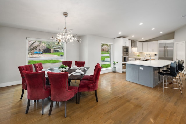 dining area with lofted ceiling, sink, an inviting chandelier, and light hardwood / wood-style flooring