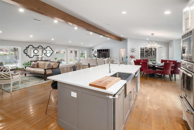 kitchen featuring appliances with stainless steel finishes, vaulted ceiling with beams, gray cabinetry, a kitchen bar, and a kitchen island with sink