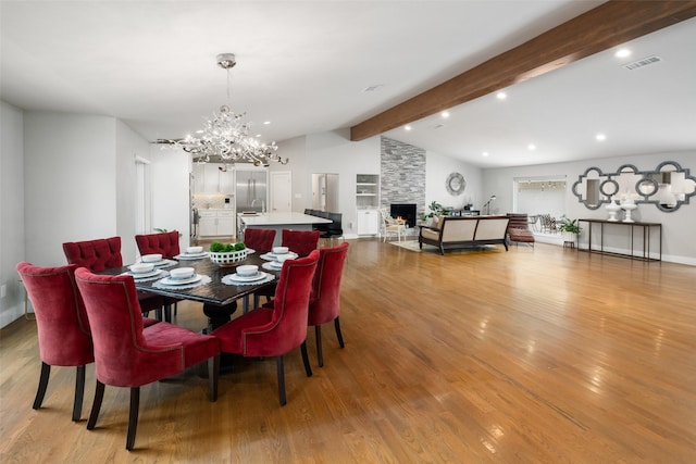 dining room with a notable chandelier, a stone fireplace, lofted ceiling with beams, and light wood-type flooring