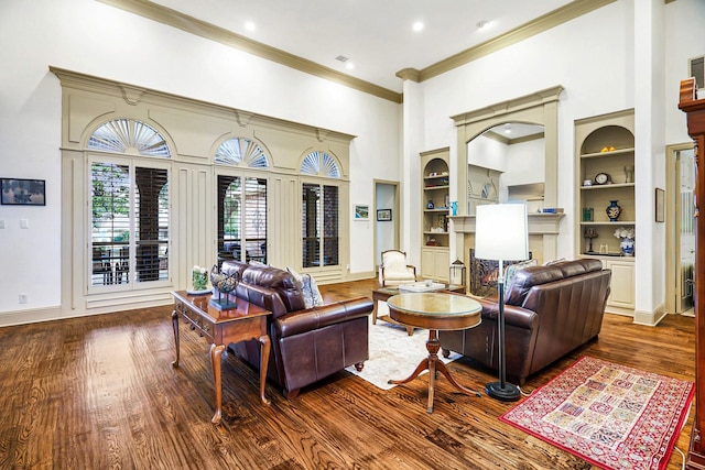 living room featuring built in shelves, a towering ceiling, crown molding, and hardwood / wood-style floors