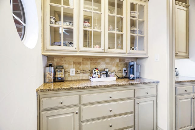 bar featuring light stone counters, decorative backsplash, and cream cabinetry