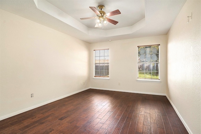 empty room with ceiling fan, dark hardwood / wood-style floors, and a raised ceiling