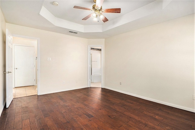 empty room with dark wood-type flooring, ceiling fan, and a tray ceiling