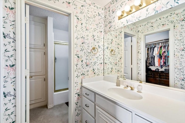 bathroom featuring vanity, enclosed tub / shower combo, and a textured ceiling