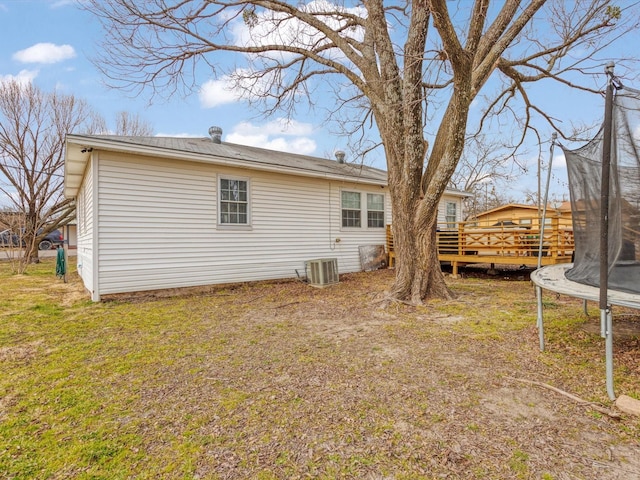 back of house featuring a wooden deck, a yard, and a trampoline