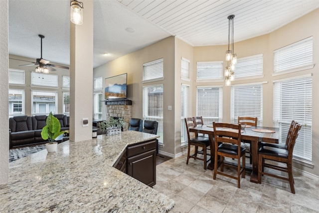 kitchen featuring dark brown cabinetry, hanging light fixtures, ceiling fan, a fireplace, and light stone countertops