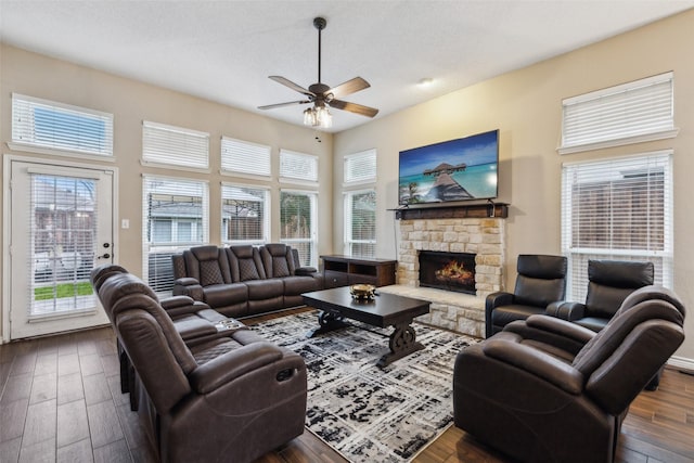 living room with a stone fireplace, a textured ceiling, dark hardwood / wood-style floors, ceiling fan, and a high ceiling