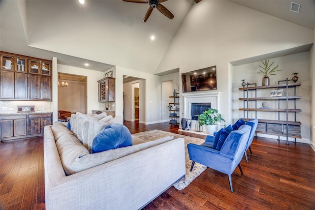 living room with dark wood-type flooring, ceiling fan with notable chandelier, and high vaulted ceiling