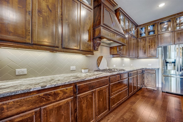 kitchen featuring dark wood-type flooring, premium range hood, appliances with stainless steel finishes, light stone countertops, and decorative backsplash