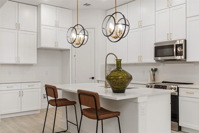 kitchen with stainless steel appliances, decorative light fixtures, an island with sink, and white cabinets