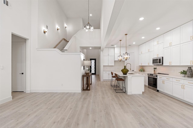 kitchen with a breakfast bar area, appliances with stainless steel finishes, white cabinetry, hanging light fixtures, and an island with sink