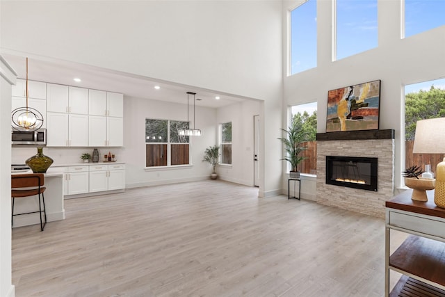 living room featuring a towering ceiling, a notable chandelier, a fireplace, and light hardwood / wood-style floors