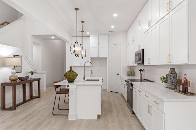 kitchen featuring decorative light fixtures, sink, white cabinets, a kitchen island with sink, and stainless steel appliances