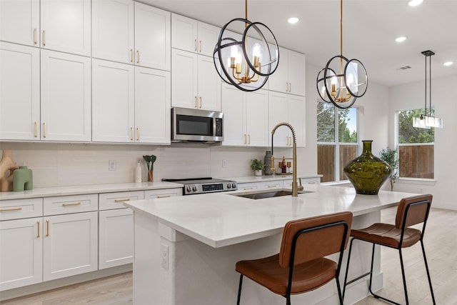 kitchen with pendant lighting, an island with sink, sink, white cabinets, and stainless steel appliances