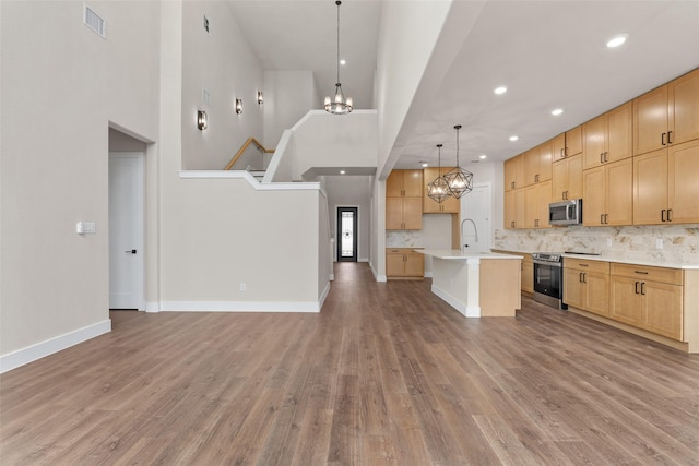 kitchen featuring pendant lighting, appliances with stainless steel finishes, wood-type flooring, an island with sink, and a chandelier