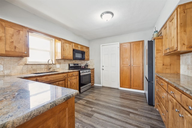 kitchen with appliances with stainless steel finishes, sink, backsplash, light stone counters, and dark wood-type flooring