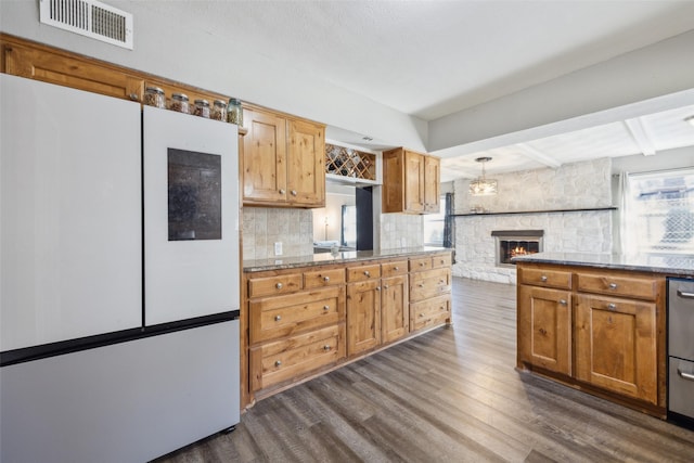 kitchen featuring dark wood-type flooring, hanging light fixtures, white refrigerator, decorative backsplash, and a stone fireplace