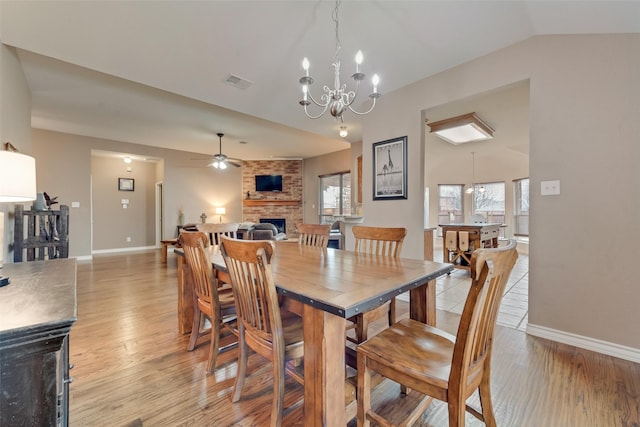 dining space with ceiling fan with notable chandelier, a fireplace, light hardwood / wood-style floors, and vaulted ceiling