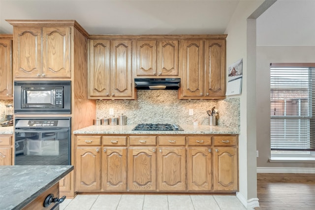 kitchen with light stone countertops, decorative backsplash, and black appliances