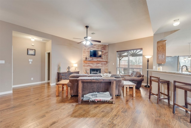 living room with ceiling fan, light wood-type flooring, sink, and a fireplace