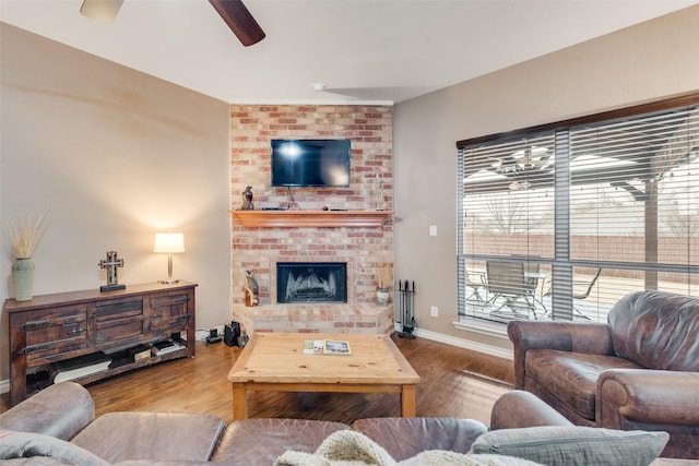 living room with a brick fireplace, wood-type flooring, and ceiling fan