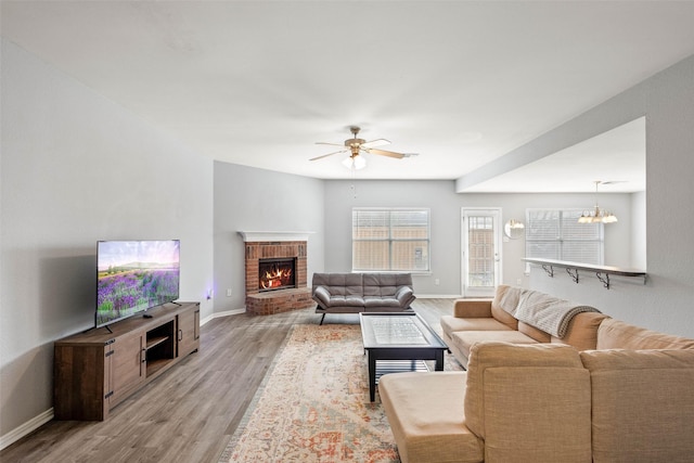 living room with a brick fireplace, ceiling fan with notable chandelier, and light hardwood / wood-style floors