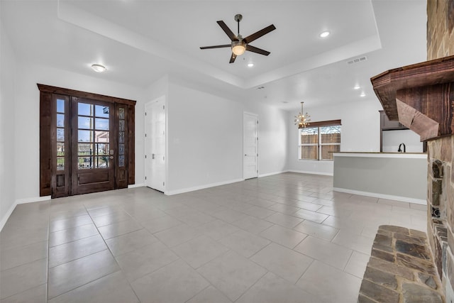 unfurnished living room with a raised ceiling, ceiling fan with notable chandelier, and light tile patterned floors