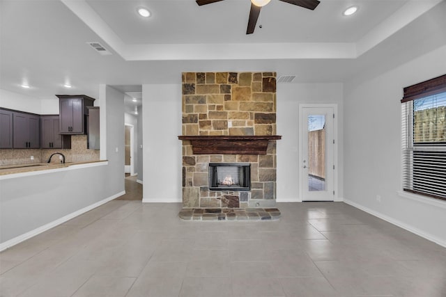 unfurnished living room with light tile patterned flooring, ceiling fan, a stone fireplace, and a raised ceiling