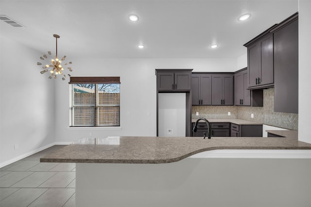 kitchen with tasteful backsplash, hanging light fixtures, sink, and kitchen peninsula