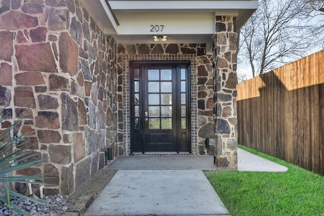 doorway to property featuring stone siding, fence, and brick siding