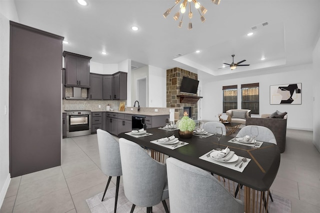 dining space with ceiling fan, a fireplace, a raised ceiling, and light tile patterned floors